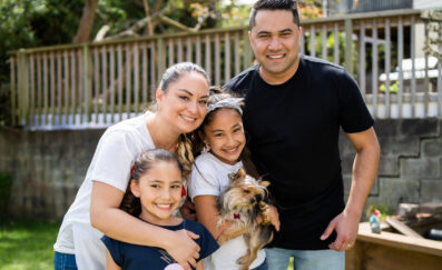 Image of family in backyard with dog. Father, mother and two daughters happy