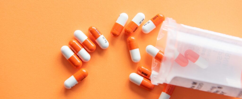 birdseye shot of light orange background with darker orange and white pills spilled out from a clear medicine canister